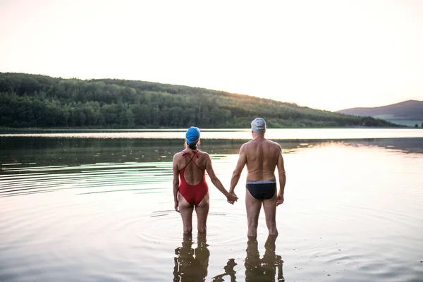 游泳前穿着泳衣站在湖中的老夫妇的背景图. — 图库照片