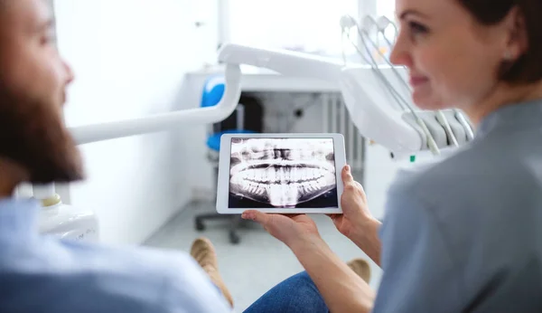 Вид ззаду стоматолога, що розмовляє з чоловіком у стоматологічній хірургії, огляд зубів . — стокове фото