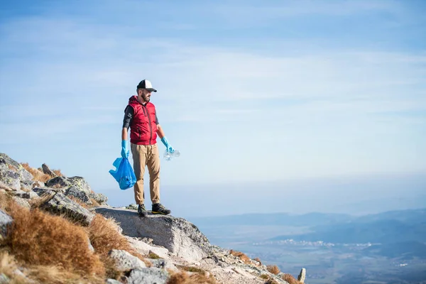 Man hiker picking up litter in nature in mountains, plogging concept. — Stock Photo, Image