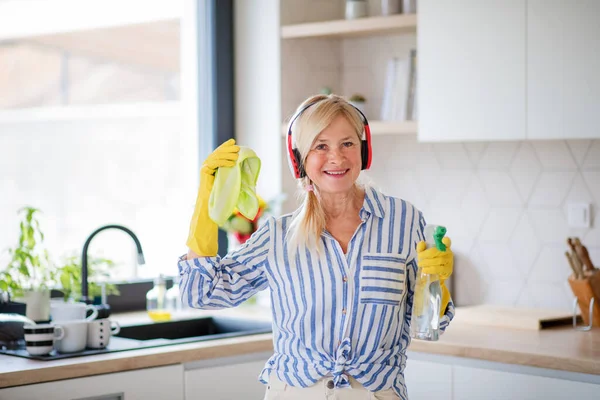 Retrato de mujer mayor con auriculares y guantes de limpieza en el interior de casa . — Foto de Stock
