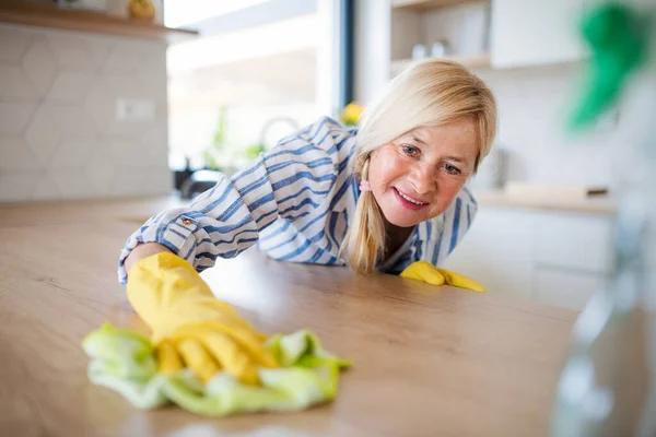 Retrato de mujer mayor limpiando el mostrador de cocina en el interior de casa . —  Fotos de Stock