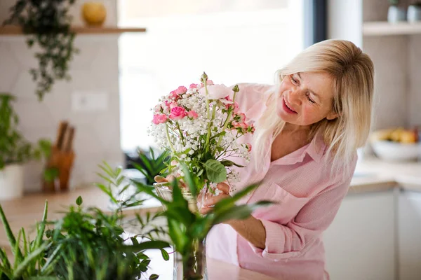 Portrait of senior woman arranging flowers in vase indoors at home. — Stock Photo, Image