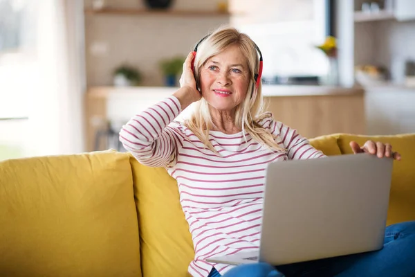 Oudere vrouw met koptelefoon en laptop binnen in het thuiskantoor, ontspannen. — Stockfoto