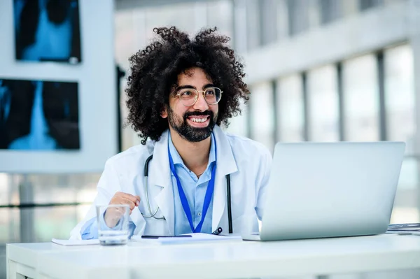 Retrato de médico masculino alegre sentado no hospital, usando laptop . — Fotografia de Stock