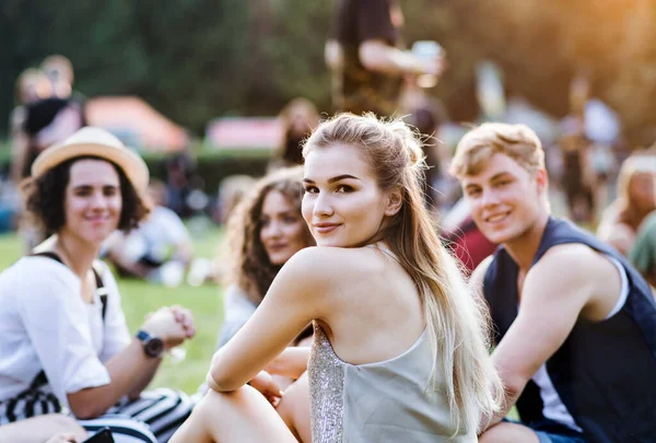 Group of young friends sitting on ground at summer festival. — Stock Photo, Image