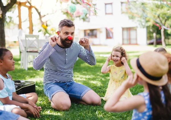 Hombre con niños pequeños en el suelo al aire libre en el jardín en verano, jugando . —  Fotos de Stock