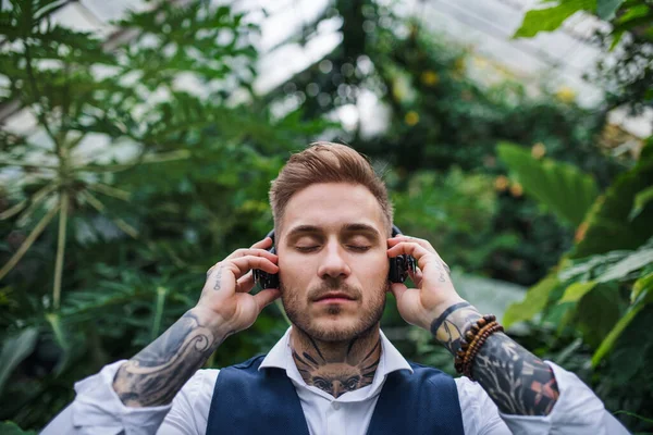 Young man with headphones standing in greenhouse in botanical garden. — Stock Photo, Image