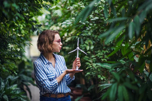 Junge Frau steht im botanischen Garten und hält Windmühlenmodell in der Hand. — Stockfoto