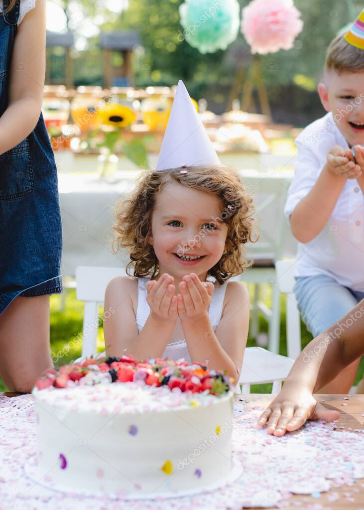 Small girl with cake celebrating birthday outdoors in garden in summer, party concept.