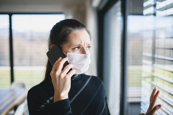 Bezorgde vrouw met telefoon en gezichtsmaskers binnen thuis, Corona virus concept. — Stockfoto