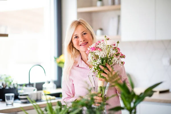 Retrato de mujer mayor arreglando flores en jarrón en el interior de casa . — Foto de Stock