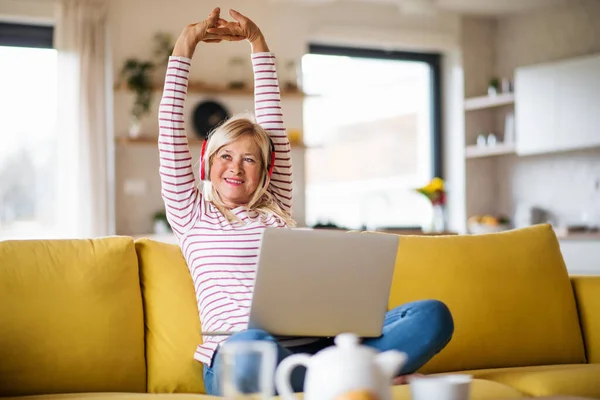 Senior kvinna med hörlurar och laptop inomhus i hemmakontoret, avkopplande. — Stockfoto