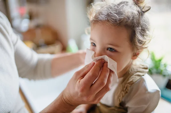Pai irreconhecível soprando nariz de pequena filha doente dentro de casa . — Fotografia de Stock