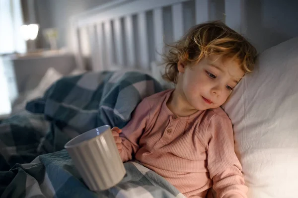 Piccola bambina malata sdraiata nel letto al chiuso a casa, in possesso di tazza . — Foto Stock