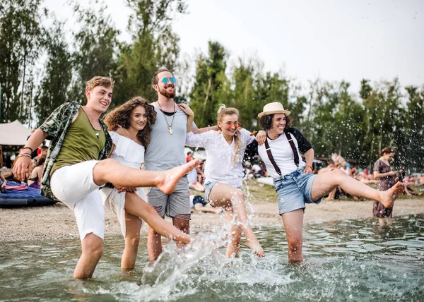 Grupa młodych przyjaciół na letnim festiwalu, stojąca nad jeziorem. — Zdjęcie stockowe