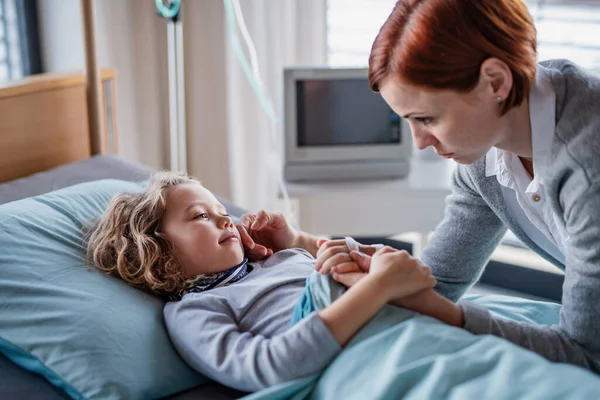 Caring mother visiting small girl daughter in bed in hospital. — Stock Photo, Image