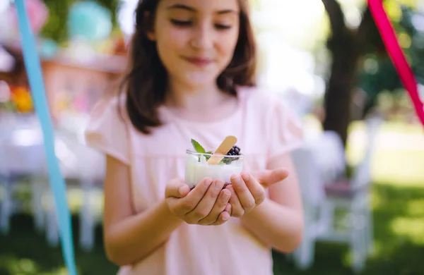 Vue de face de la petite fille en plein air dans le jardin en été, tenant le dessert dans la tasse . — Photo