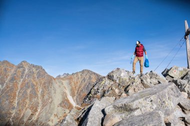 Man hiker picking up litter in nature in mountains, plogging concept.