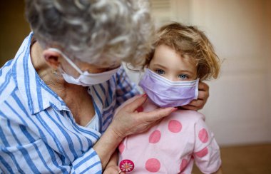 Evde yüz maskesi takan büyükanne ve küçük kız. Corona virüsü ve karantina konsepti..