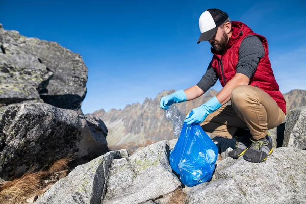 Man hiker picking up litter in nature in mountains, plogging concept. — ストック写真