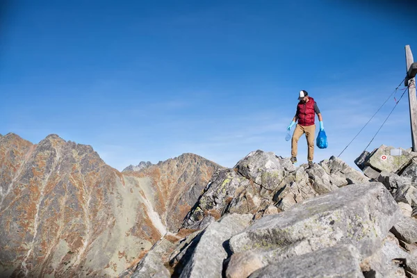 Man hiker picking up litter in nature in mountains, plogging concept. — Stockfoto