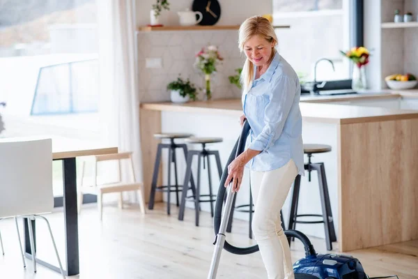 Portrait of senior woman with vacuum cleaner indoors at home, hoovering. — Stock Photo, Image
