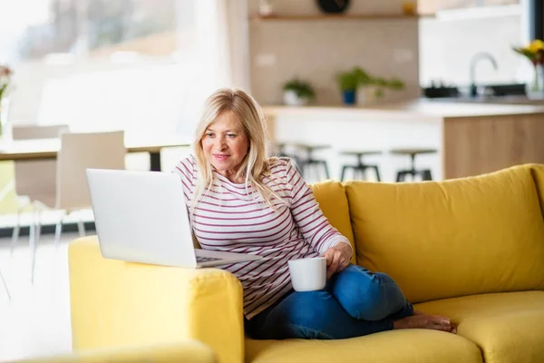 Mulher sênior com café e laptop em casa, relaxante . — Fotografia de Stock