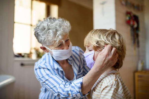 Mujer y niño pequeño con mascarilla interior en casa, virus corona y concepto de cuarentena . —  Fotos de Stock