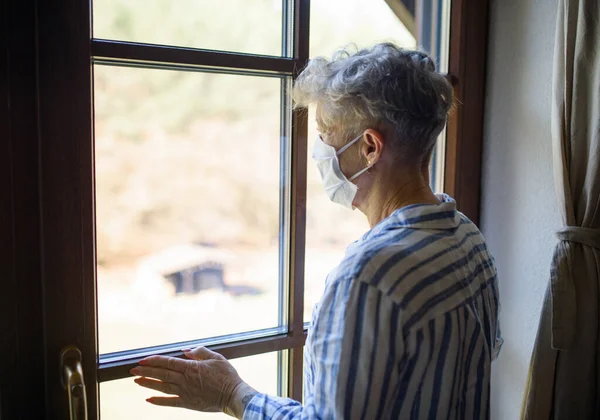 Θλιβερή ηλικιωμένη γυναίκα με μάσκα προσώπου σε εσωτερικούς χώρους στο σπίτι, ιός κορώνας και καραντίνα έννοια. — Φωτογραφία Αρχείου