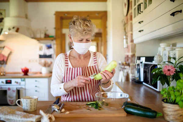 Woman with face mask and gloves cooking indoors at home, corona virus concept. — Stock Photo, Image