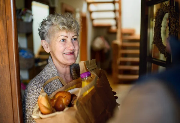 Oigenkännlig kurir levererar shopping till senior kvinna, corona virus och karantän koncept. — Stockfoto