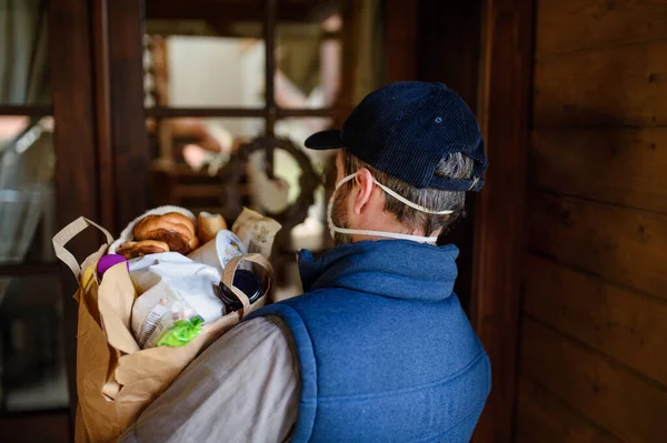 Bakifrån av kurir med ansiktsmask leverera shopping, corona virus och karantän koncept. — Stockfoto