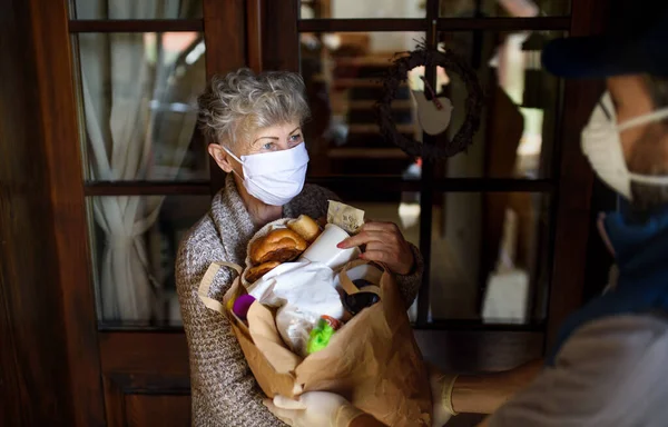 Courier delivering shopping to senior woman with face mask, corona virus and quarantine concept. — Stock Photo, Image