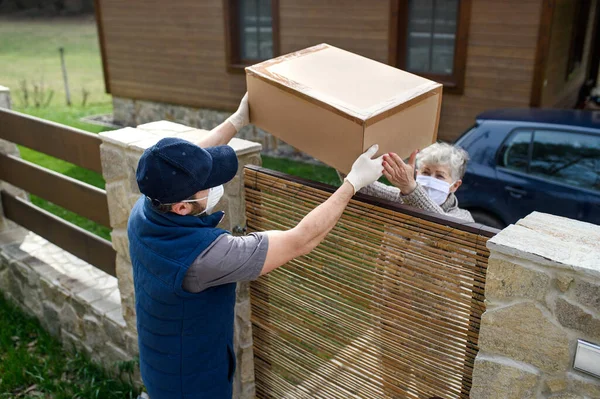 Courier delivering parcel to senior woman with face mask, corona virus and quarantine concept. — Stock Photo, Image