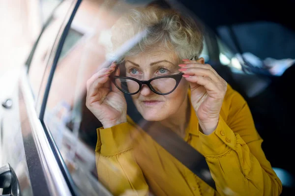 En äldre kvinna med glasögon i en bil. Skjuten genom glas. — Stockfoto