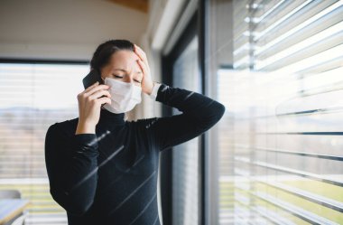 Evde telefon ve yüz maskeleri olan endişeli kadın, Corona virüsü konsepti..