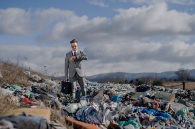 Modern businessman on landfill, consumerism versus pollution concept. clipart