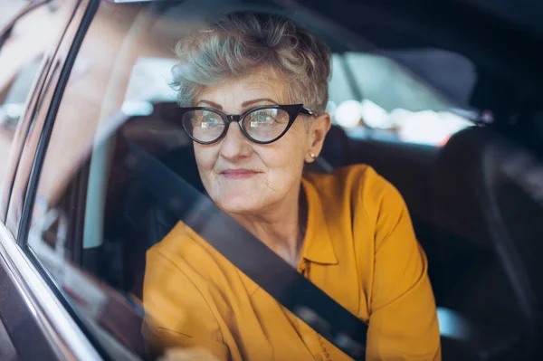 Mujer mayor con gafas sentada en un coche. Disparo a través de vidrio . — Foto de Stock