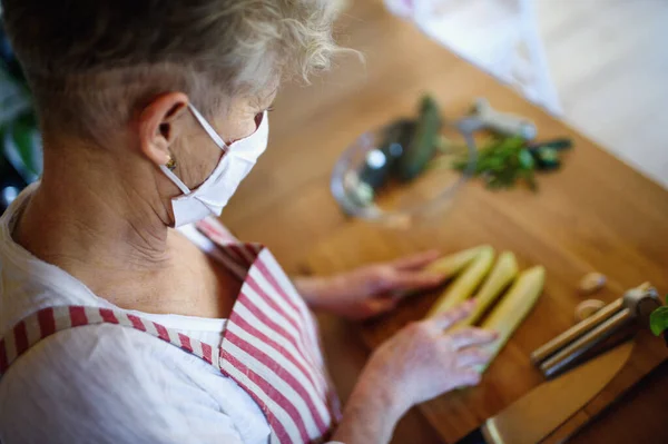 Vrouw met gezichtsmasker koken binnen thuis, corona virus concept. — Stockfoto