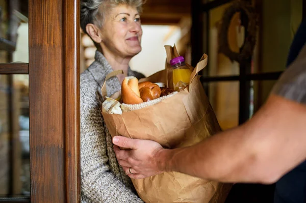 Mensajero irreconocible entregando compras a una mujer mayor . — Foto de Stock