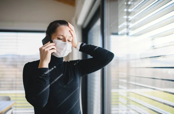 Femme inquiète avec téléphone et masques à l'intérieur à la maison, concept de virus Corona . — Photo