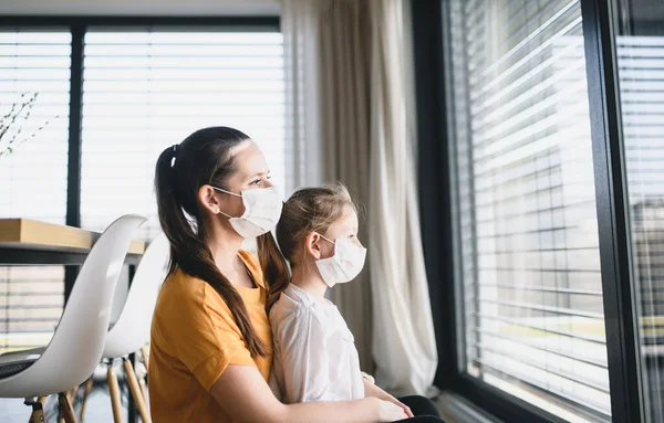 Moeder en kind met gezichtsmaskers binnenshuis, Corona virus en quarantaine concept. — Stockfoto