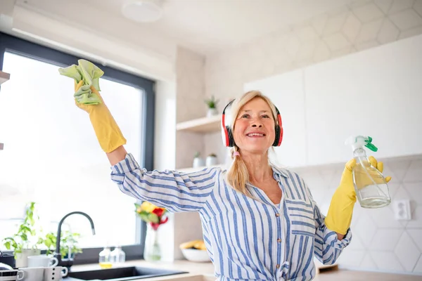 Portrait of senior woman with headphones and gloves cleaning indoors at home. — Stock Photo, Image