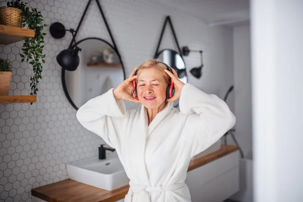 Retrato de mujer mayor con auriculares y albornoz en casa . — Foto de Stock