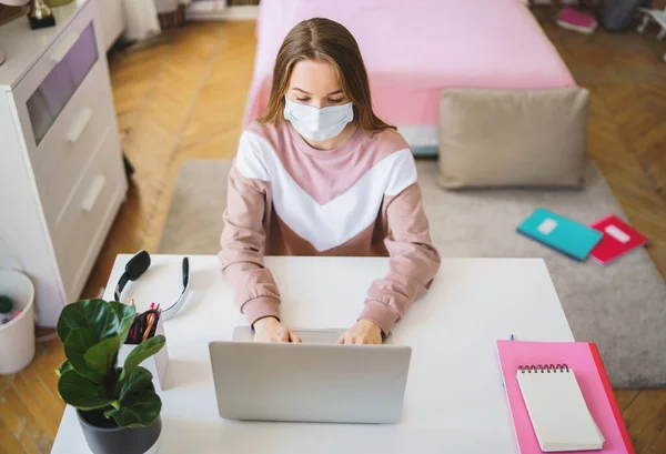 Jovem estudante com máscara facial na mesa, usando laptop em quarentena . — Fotografia de Stock