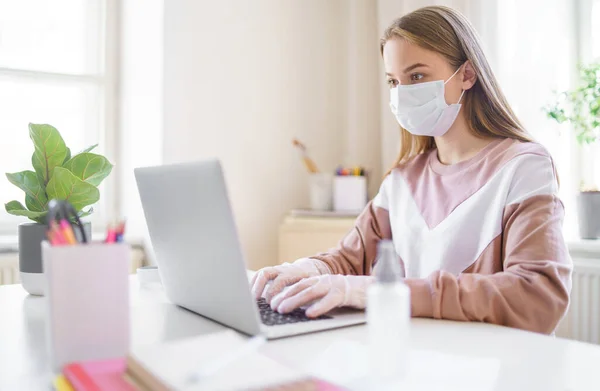 Joven estudiante con mascarilla en la mesa, usando laptop en cuarentena . — Foto de Stock