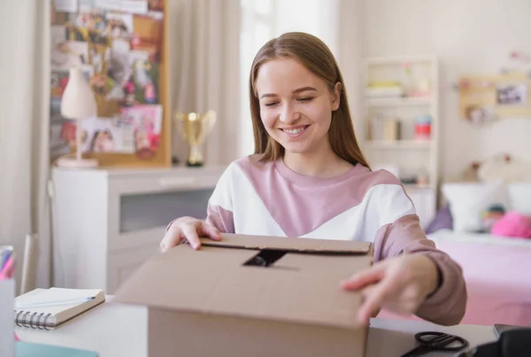 Junge Studentin sitzt am Tisch und öffnet Paketkasten. — Stockfoto