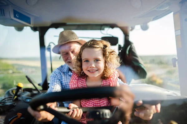 Fermier âgé avec sa petite-fille assise dans un tracteur, conduisant . — Photo