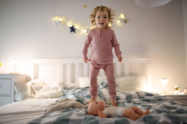 Pequeña niña saltando en la cama en casa, divirtiéndose . — Foto de Stock