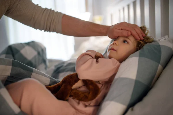 Father checking forehead of small sick toddler daughter indoors at home. — Stock Photo, Image